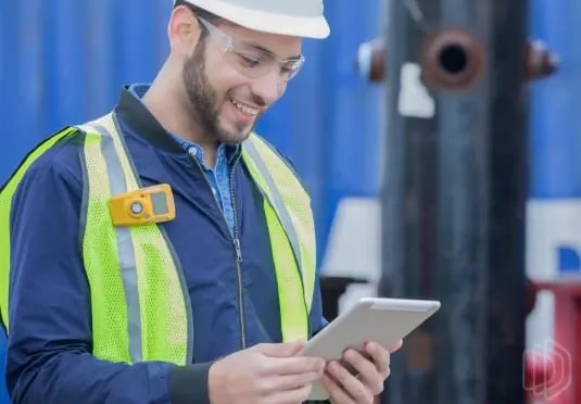 A field technician in safety gear looking at a tablet